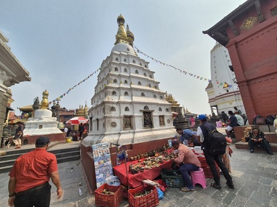 Poh�ad na bielu ve�ovit� st�pu Anantapur so zlat�m vrcholom a modlitebn�mi vlajo�kami v budhistickom komplexe Swayambhunath. Pred st�pou pred�va miestny mu� suven�ry rozlo�en� na stol�ku.