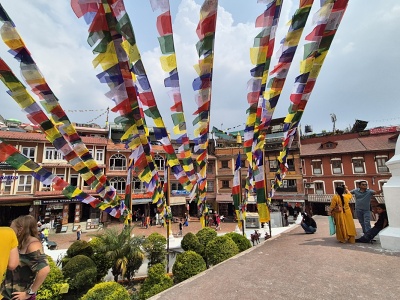 Detailn� poh�ad na pestrofarebn� budhistick� modlitebn� vlajo�ky lungta ve�aj�ce sa v l��och z terasy st�py Boudhanath, s v�h�adom na tradi�n� tehlov� budovy, kaviarensk� terasy a n�v�tevn�kov na n�mest� v K�thm�ndu.