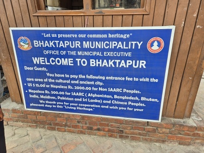Modr� informa�n� tabu�a mesta Bhaktapur pri drevenej pokladni s cenn�kom vstupn�ho a priv�tan�m pre zahrani�n�ch turistov pred vstupom do pamiatkovej z�ny Svetov�ho dedi�stva UNESCO.