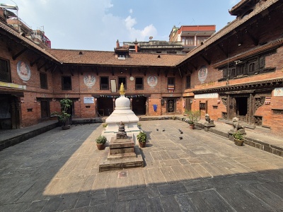 Tradi�n� tehlov� n�dvorie m�zea Patan Museum s malou bielou st�pou chorten uprostred, obklopen� historick�mi budovami s vyrez�van�mi dreven�mi oknami a ma�bami bo�stiev na fas�de.