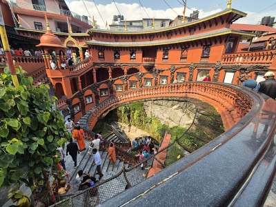 Poh�ad zhora na �pir�lovit� schodisko a ozdobn� �erven� architekt�ru ved�cu do podzemnej jaskyne Gupteshwor Mahadev Cave pri vodop�de Devi's Fall v Pokhare, s n�v�tevn�kmi kr��aj�cimi do podzemia.