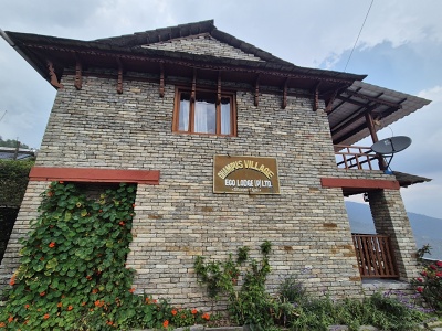 Tradi�n� kamenn� budova Dhampus Village Eco Lodge s dreven�mi oknami, balk�nom a zelen�m pop�nav�m porastom v dedine Dhampus v Nep�le.