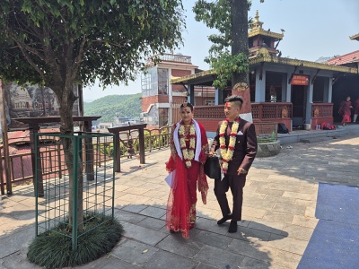 Mlad� nep�lski novoman�elia v svadobn�ch odevoch s kvetinov�mi girlandami a �erven�m znamienkom tika kr��aj�ci po dl�denom n�dvor� hinduistick�ho chr�mu Bindhyabasini v Pokhare.