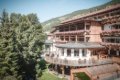 Hotel s kvetinov�mi balk�nmi a terasou pri stromoch pod zalesnen�m svahom