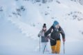 Dvojica turistov s palicami kr��a hlbok�m snehom pod skalnat�m svahom