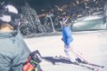 Ly�iari na osvetlenej zjazdovke so zasne�en�mi stromami a svetlami obce v pozad�