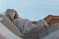 �ena v bielom �upane s uter�kom na hlave odpo��va na le�adle pred v�h�adom na more