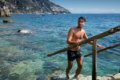 Mu� v plavk�ch vystupuje z mora po schodoch s dreven�m z�bradl�m