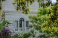 Biela fas�da s obl�kov�m oknom a balustr�dou medzi zelen�mi stromami