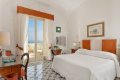 Izba s oran�ovo-bielym �elom postele a presklen�mi dverami s v�h�adom na more