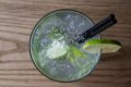 Koktail s drven�m �adom, limetkou a dvoma �iernymi slamkami na drevenom stole
