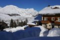 Budova s dreven�mi balk�nmi pod snehom a horsk� �t�ty nad �dol�m