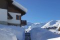 Schody medzi snehov�mi stenami pri budove s horami v pozad�