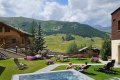 Baz�n so zv�renou vodou, �udia na le�adl�ch a zelen� horsk� svahy za z�hradou
