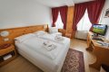 Dve spojen� l��ka, �erven� z�vesy a dreven� p�sac� st�l s telev�zorom v izbe